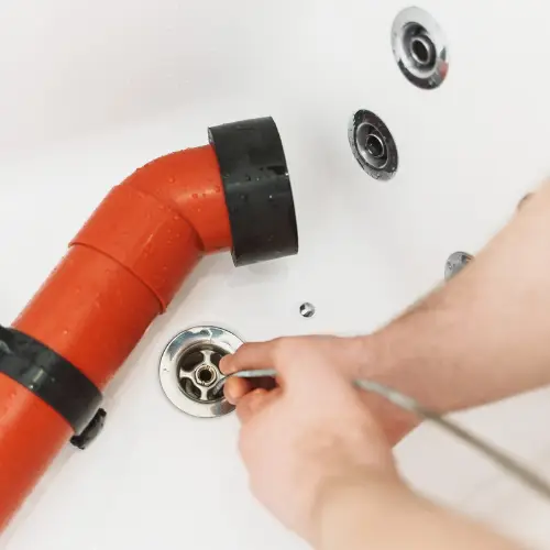 A technician feeding a drain snake cable into a tub drain