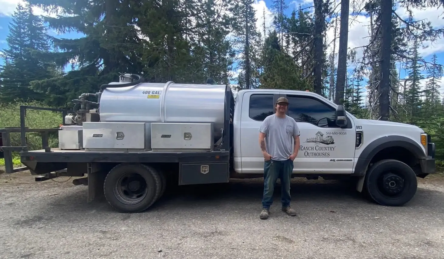 A Ranch Country Outhouses technician standing beside a service truck in the pines